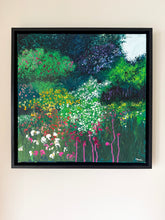 Load image into Gallery viewer, A framed abstract landscape painting of a wildflower meadow hangs on a light beige wall. The painting features textured brushstrokes of green, blue, yellow, pink, and white, enclosed in a simple black frame.
